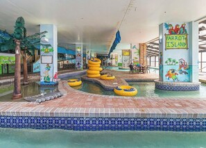 Ein Poolbereich im Innenbereich mit mehreren Wasserrutschen und aufblasbaren Ringen, umgeben von gefliesten Wänden und einem Wandbild von Papageien.