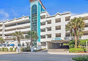 A multi-story parking garage with a blue and white facade, a clear sky, and palm trees. - Oceanfront Paradise Getaway with Amazing Views (Myrtle Beach)