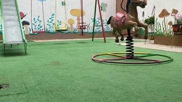 Ein Spielbereich für Kinder mit Schaukeln, einer Rutsche und einem Spielzeugpferd zum Aufsitzen.