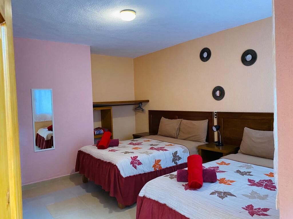 A hotel room with two beds, a mirror, a shelf, and a wall clock.