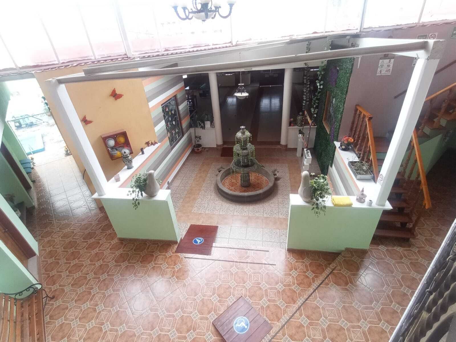 Un vestíbulo con una fuente central, una recepción y una escalera.