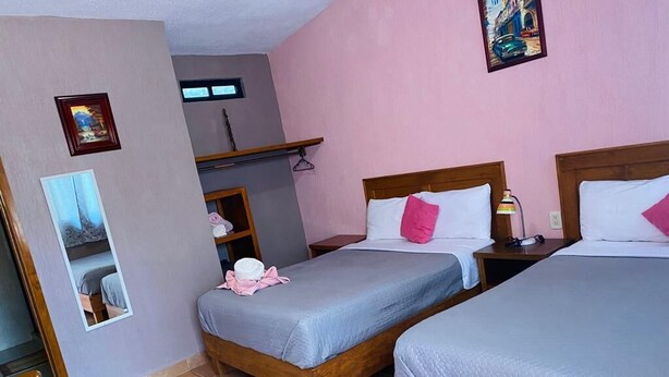 Habitación de hotel con dos camas de madera, una mesita, una silla y un espejo.