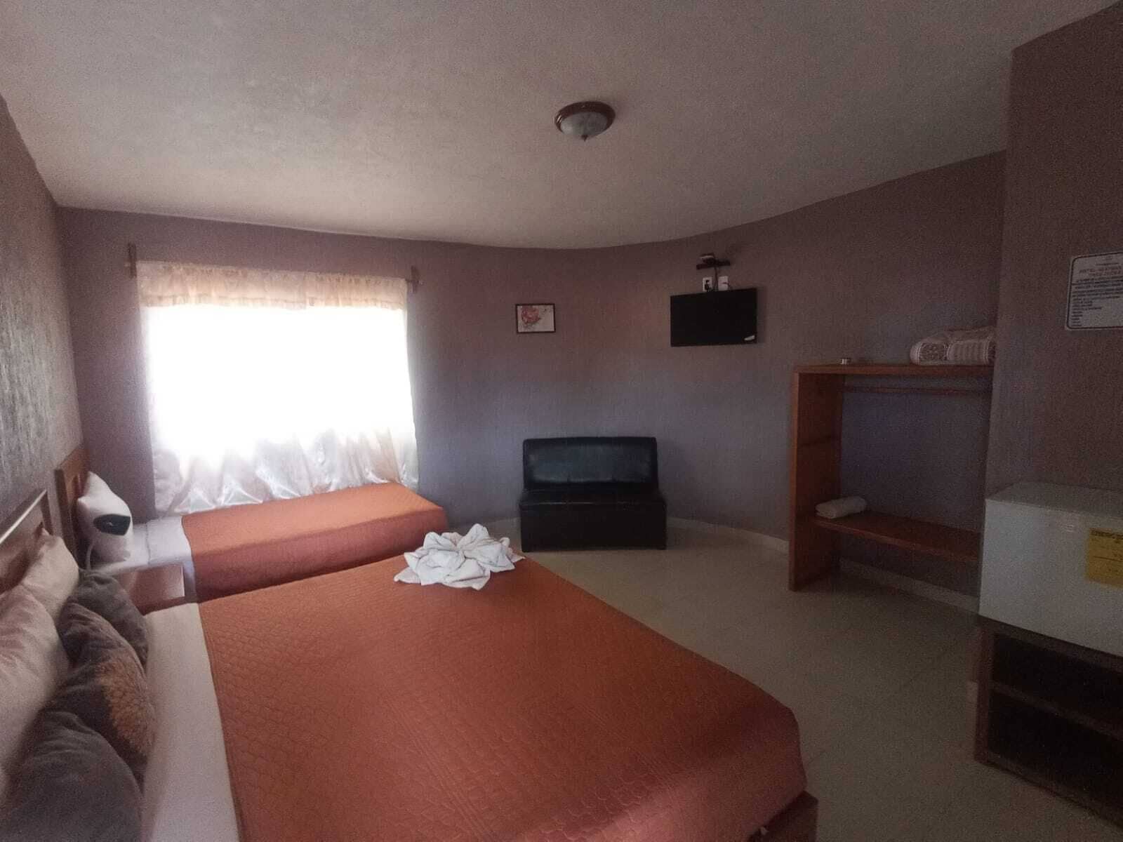 Habitación de hotel con dos camas, televisión, ventana con cortinas y un pequeño estante.
