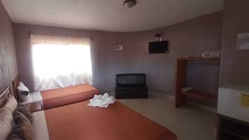 Habitación de hotel con dos camas, televisión, ventana con cortinas y un pequeño estante.
