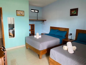 Una habitación con dos camas de madera, cada una con cubrecama gris y almohadas azules, y una pequeña mesa con una silla.