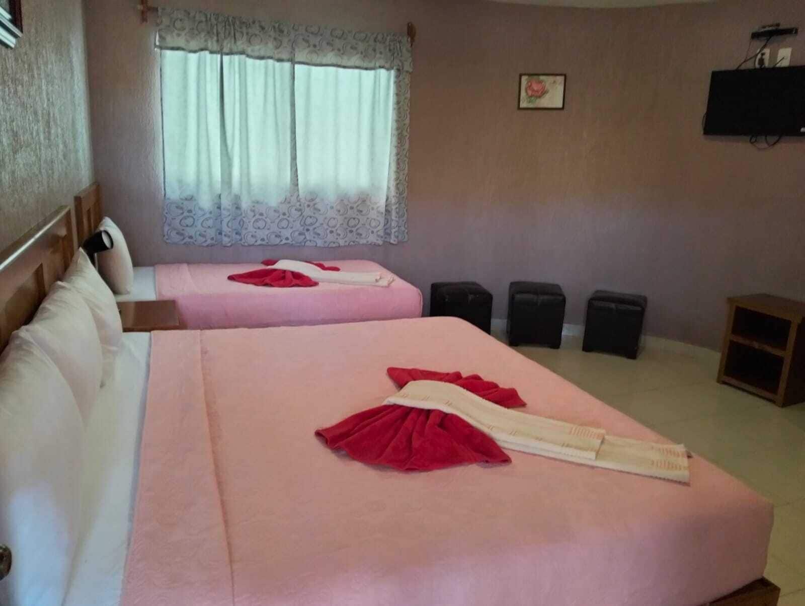 Habitación de hotel con dos camas, una ventana con cortinas, un televisor en la pared y un pequeño armario de madera.
