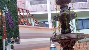 Un atrio de varios niveles con una fuente de piedra central, una escalera y una pared decorativa con plantas.