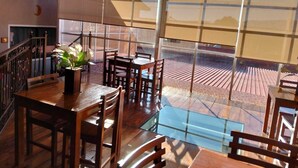 Un comedor con una mesa y sillas de madera, una planta en maceta y vistas a una terraza exterior a través de amplios ventanales.