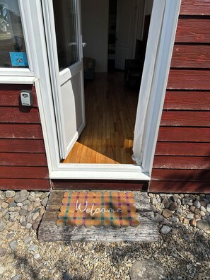 Eine Holzhütte mit Schiebeglastür, Fußmatte und einem Kiesweg.