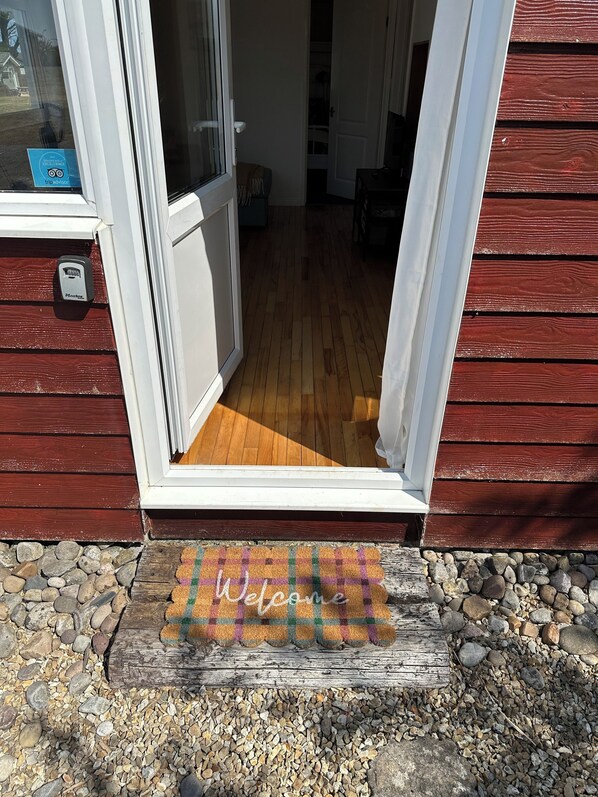 A wooden cabin with a sliding glass door, a welcome mat, and a stone pathway.