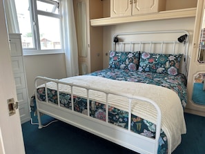 Ein Bett mit weißem Metallgestell, einer blumigen Tagesdecke und passendem Kopfkissen.