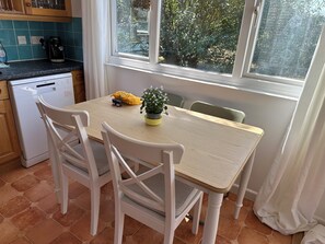 A kitchen with a dishwasher, a table with chairs, a potted plant, and a window with a view of trees.