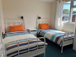 Two single beds with metal frames, white bedding, and orange pillows.
