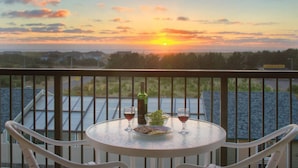Un balcon avec une table dressée pour deux personnes, une bouteille de vin et un panier de raisins.