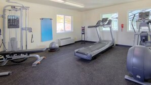 Une salle de sport équipée de divers appareils, notamment un tapis de course, un vélo elliptique et des appareils de musculation.
