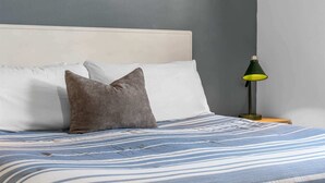 Ein Bett mit gestreifter Bettdecke, einem Kopfkissen und einem Nachttisch mit Lampe.