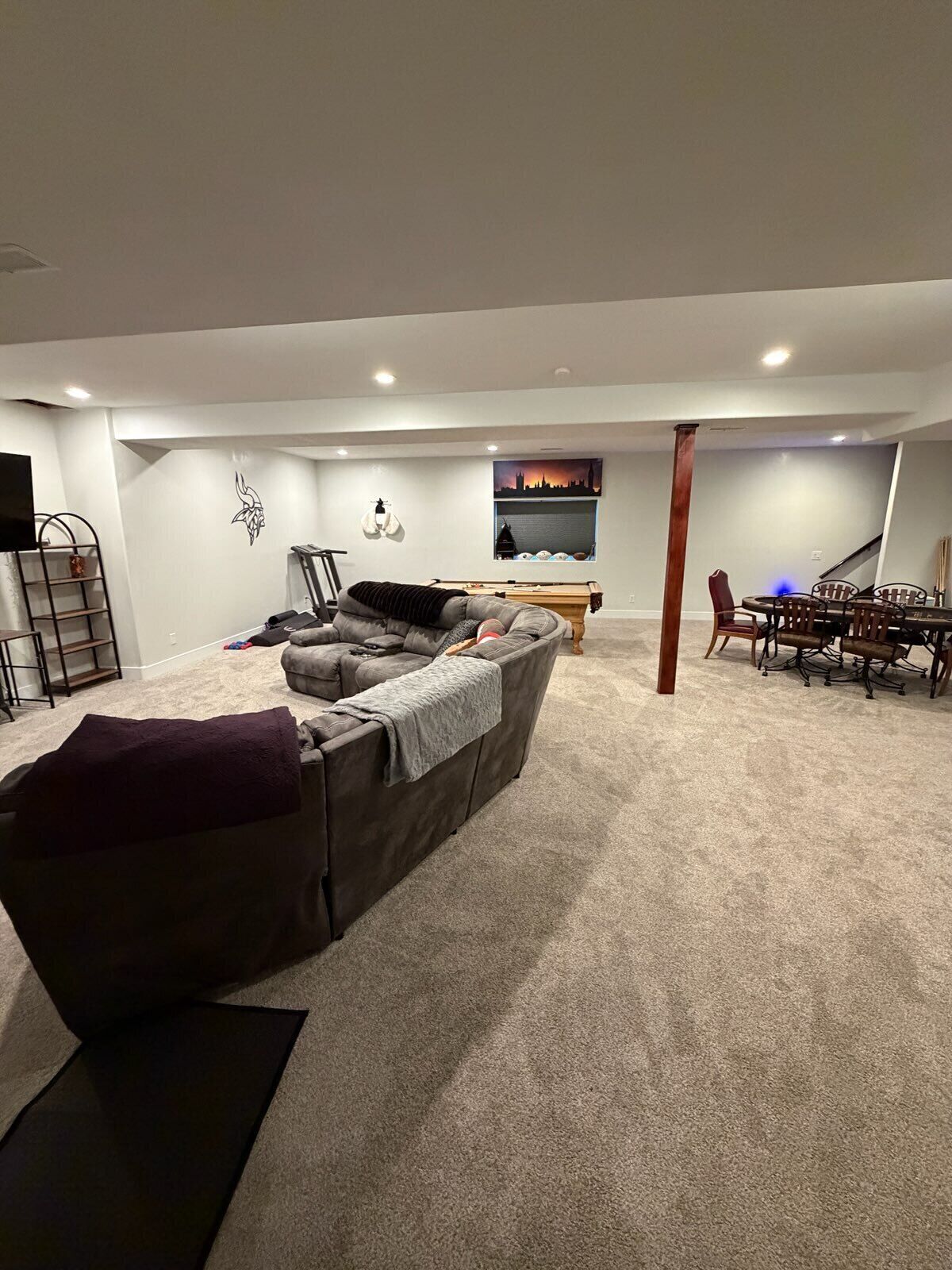 A living room with a grey sofa, a dining table with chairs, a TV, and a wall-mounted shelf.