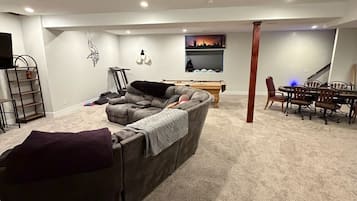 A living room with a grey sofa, a dining table with chairs, a TV, and a wall-mounted shelf.