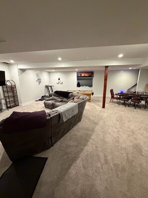 A living room with a grey sofa, a dining table with chairs, a TV, and a wall-mounted shelf.