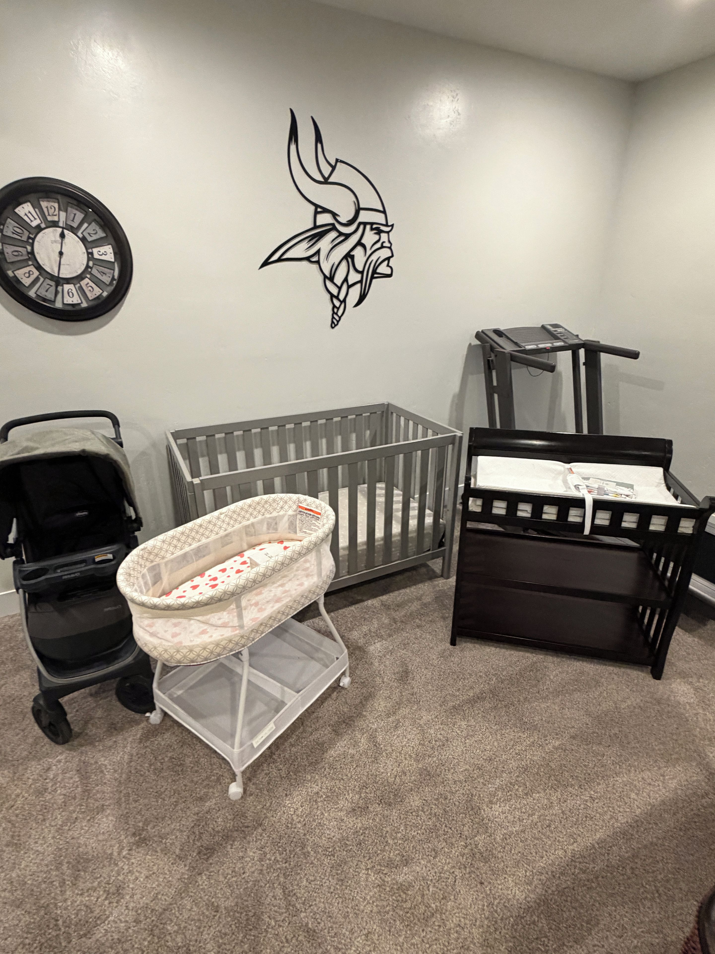 A baby room with a crib, a changing table, a stroller, and a wall clock.