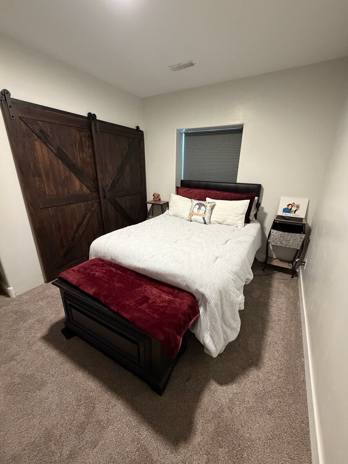 A bedroom with a bed, a nightstand, a window with blinds, and a sliding door.