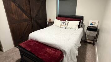 A bedroom with a bed, a nightstand, a window with blinds, and a sliding door.
