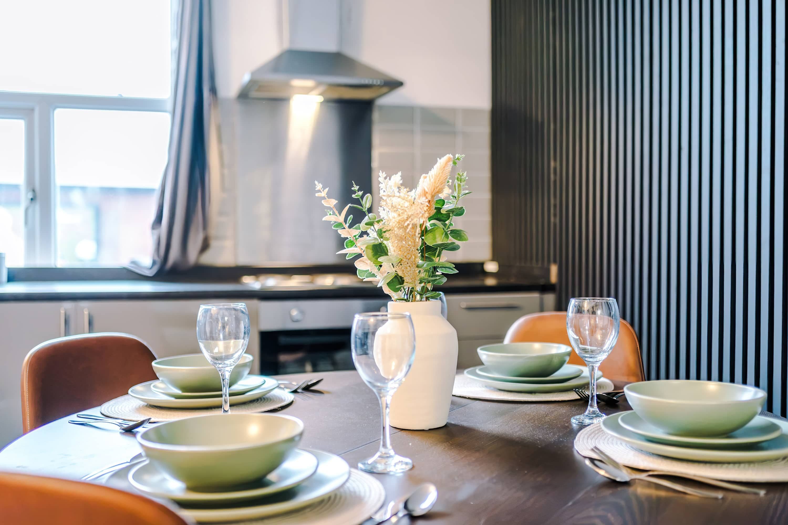 A dining table set with plates, bowls, and wine glasses, with a vase of flowers in the center.