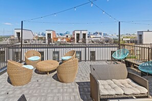 Eine Dachterrasse mit Korbmöbeln, Blick auf den Stadt-Horizont und Lichterketten.