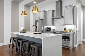 A modern kitchen with a central island, stainless steel appliances, and bar stools. - Luxury 8BR Nashville Stay • 2 Rooftops + City Views + Fire Pits (Nashville)