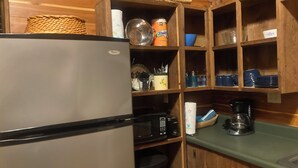 A compact kitchen with a refrigerator, microwave, and coffee maker. Wooden shelves hold various kitchen items and utensils. - Adorable 1-bedroom cabin in Treat, Arkansas.  2 adults, no pets, 2 night minimum (Dover)