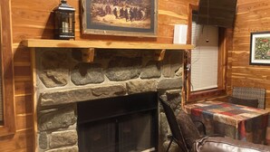 A stone fireplace with a mantel, a framed painting above it, and a quilted table nearby. - Adorable 1-bedroom cabin in Treat, Arkansas.  2 adults, no pets, 2 night minimum (Dover)
