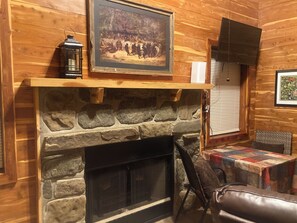 A stone fireplace with a mantel, a framed painting above it, and a quilted table nearby. - Adorable 1-bedroom cabin in Treat, Arkansas.  2 adults, no pets, 2 night minimum (Dover)