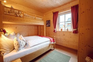 Ein Zimmer mit einem Holzbett mit Etagen, einem Fenster und einem Teddy auf dem Bett, sowie einem grünen Teppich.
