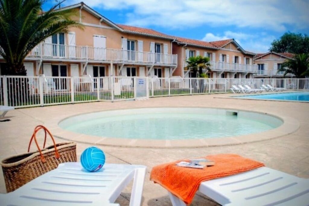 A pool area with lounge chairs, a small pool, and a building with balconies.