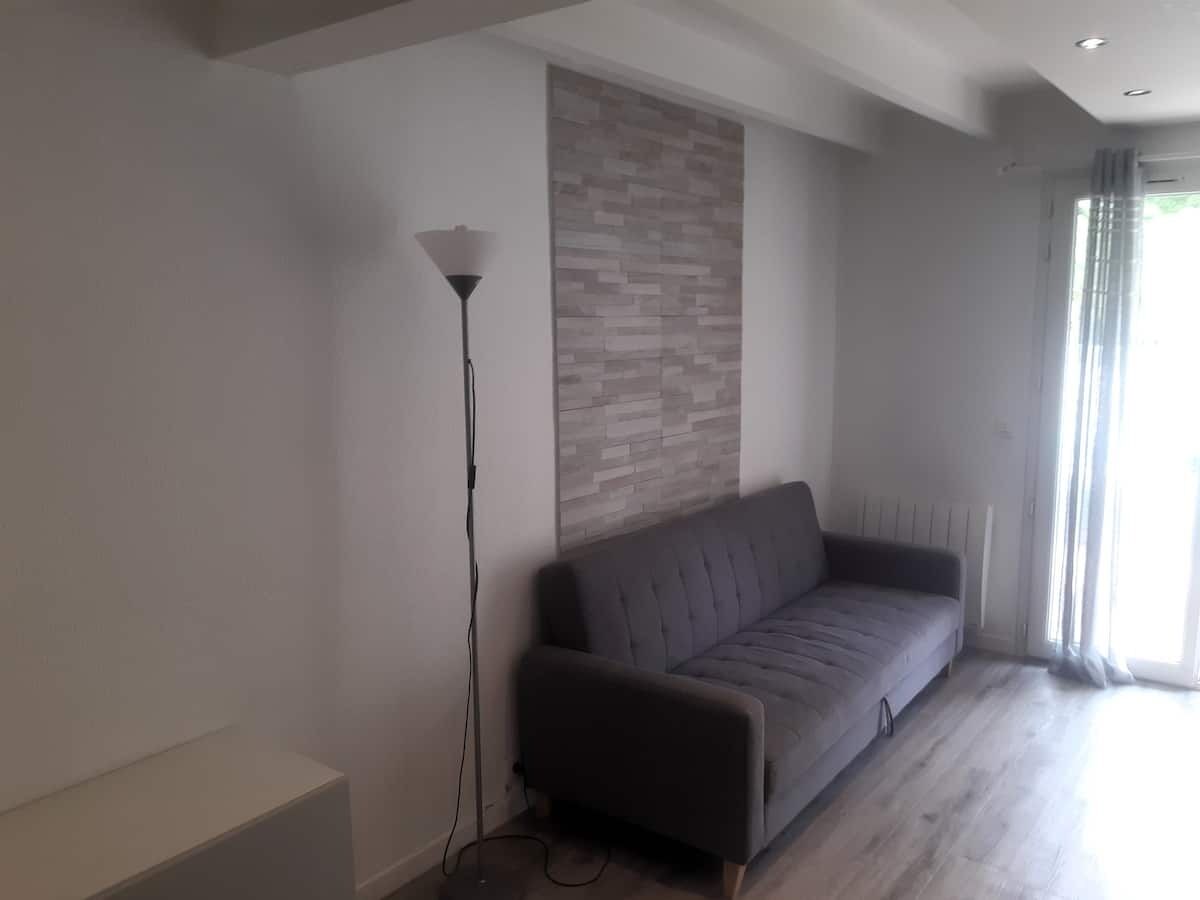 Een moderne woonkamer met een grijze bank, een vloerlamp en een wand met een structuurpatroon.