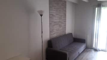 Een moderne woonkamer met een grijze bank, een vloerlamp en een wand met een structuurpatroon.