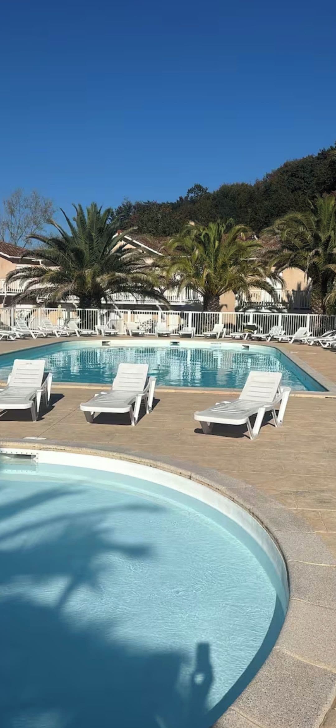 Piscina com espreguiçadeiras e cerca branca.