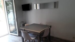 Et moderne spiseområde med et bord og stole, et tv ophængt på væggen og en skydedør, der fører til et udeområde.
