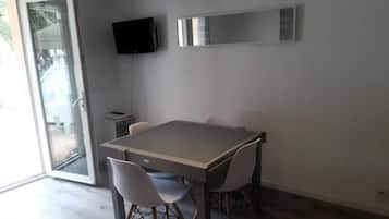 Een moderne eetruimte met een tafel en stoelen, een aan de muur bevestigde televisie en een schuifdeur naar een buitenruimte.