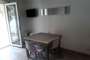 Ein zeitgemäßer Essbereich mit Tisch und Stühlen, einem an der Wand befestigten Fernseher und einer Schiebeglastür zum Außenbereich.