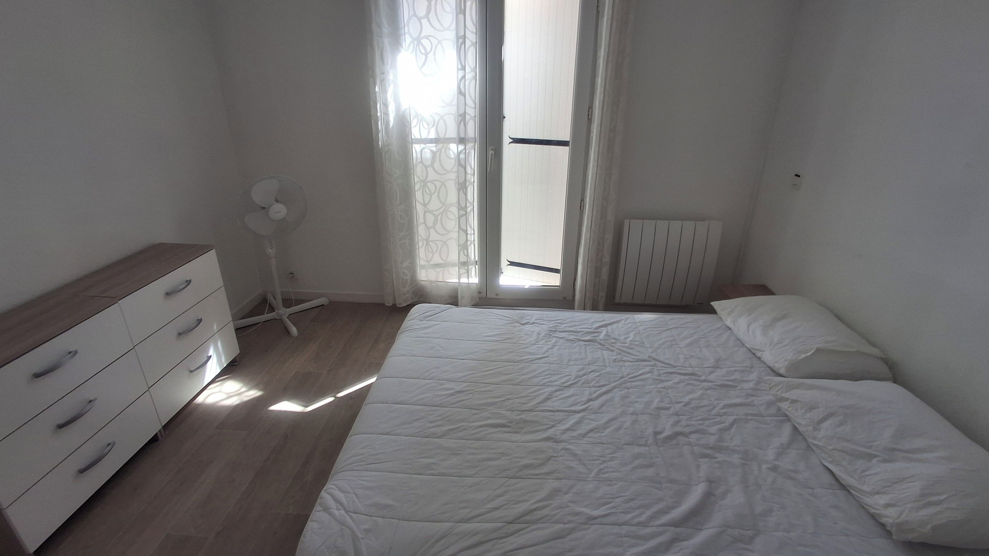 A bedroom with a bed, a dresser, a radiator, and a window with curtains.