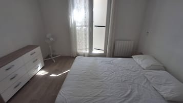 A bedroom with a bed, a dresser, a radiator, and a window with curtains.