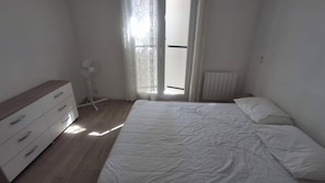 A bedroom with a bed, a dresser, a radiator, and a window with curtains. - Duplex apartment for 6 people in a residence with a pool (Anglet)