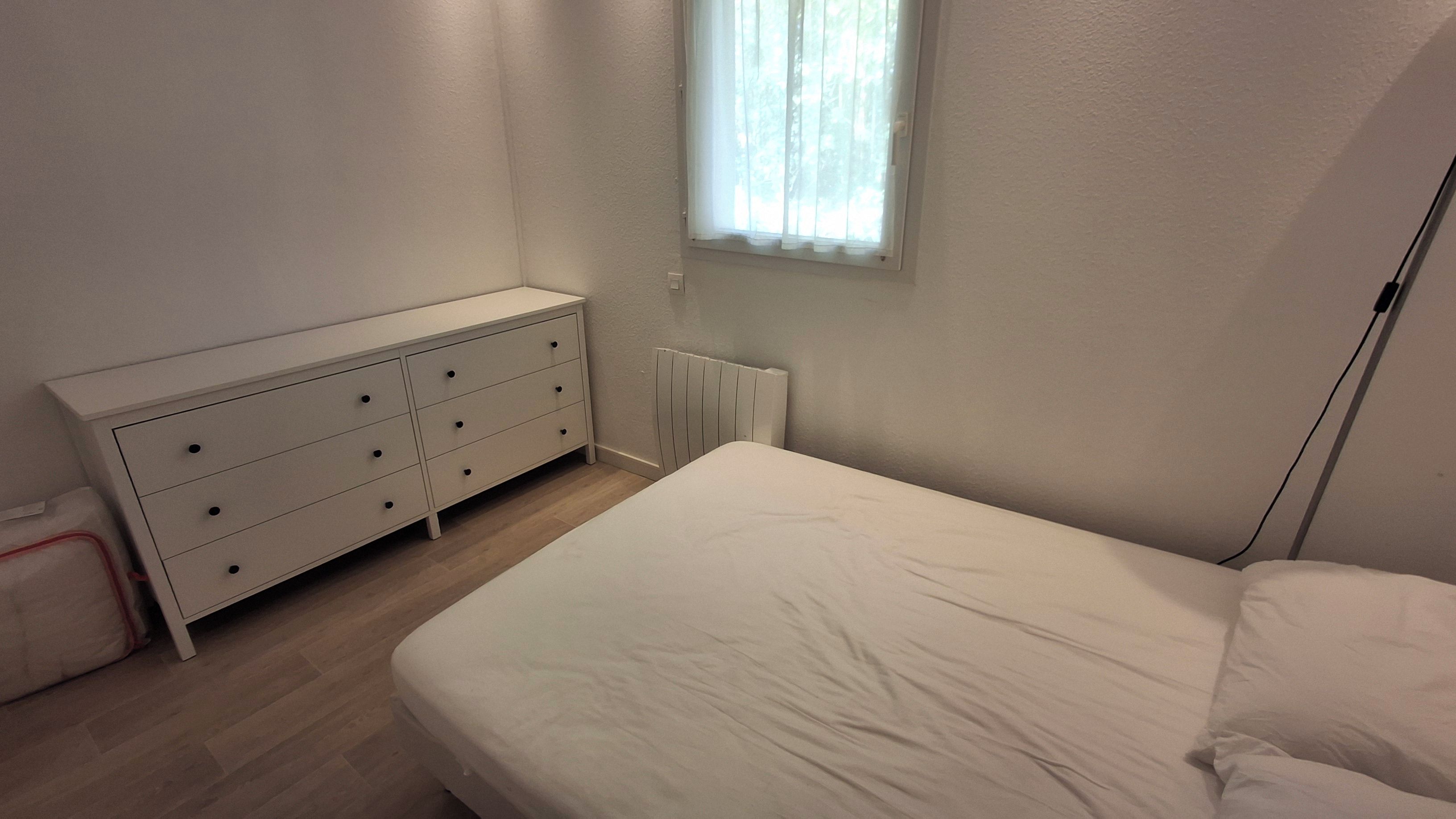 A bedroom with a bed, a dresser, a radiator, and a window with curtains.