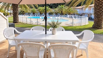 Un patio con una mesa y sillas, una piscina al fondo y una cerca blanca delimitando el espacio.