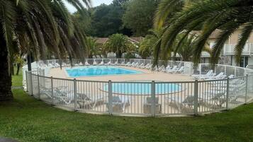 A swimming pool surrounded by a white fence, with lounge chairs and palm trees.