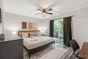 Ein Schlafzimmer mit einem Bett, Nachttischen, einem Deckenventilator, Blick durch eine Glastür und einem kleinen Balkon.