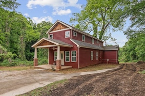 A two-story house with a covered porch, surrounded by dense greenery. - Stylish 4BR Home Near ATL Airport & Beltline (Atlanta)