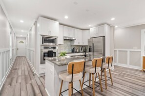 A modern kitchen with white cabinetry, stainless steel appliances, a granite countertop, and bar stools. - Stylish 4BR Home Near ATL Airport & Beltline (Atlanta)