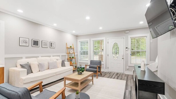 A modern living room with a sofa, coffee table, and chairs, a TV mounted on the wall, and a door with a glass panel. - Stylish 4BR Home Near ATL Airport & Beltline (Atlanta)